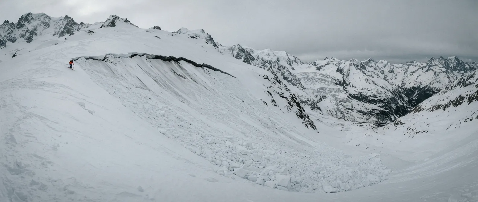 Une plaque de neige fracturée sur une pente raide, une ligne de fracture nette qui traverse le versant, un skieur minuscule en contrebas